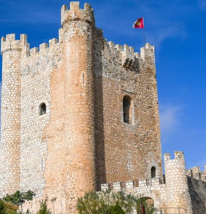 Explore the medieval architecture of Alcalá del Júcar castle under a clear blue sky.