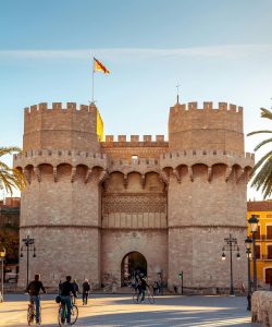 Historic Serranos Towers in Valencia, Spain under a clear blue sky with people and cyclists in the foreground.