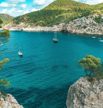Sailboats drift in a stunning turquoise bay surrounded by rocky cliffs in Ibiza, Spain.