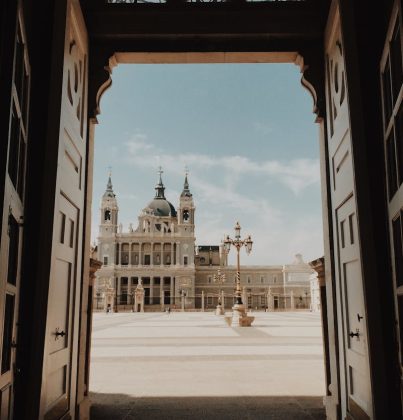A stunning view of Madrid's Almudena Cathedral framed by an ornate doorway from the Royal Palace.